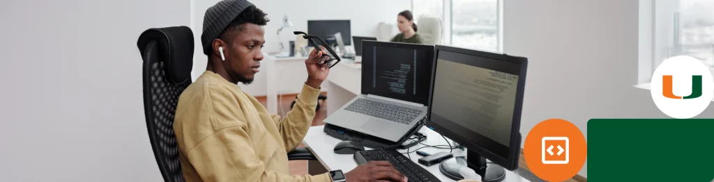 Person sitting at a desk with multiple screens, coding, in an office environment