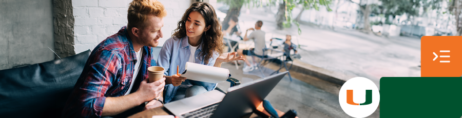 "Two people discussing work on a couch with a laptop, in a bright café setting."